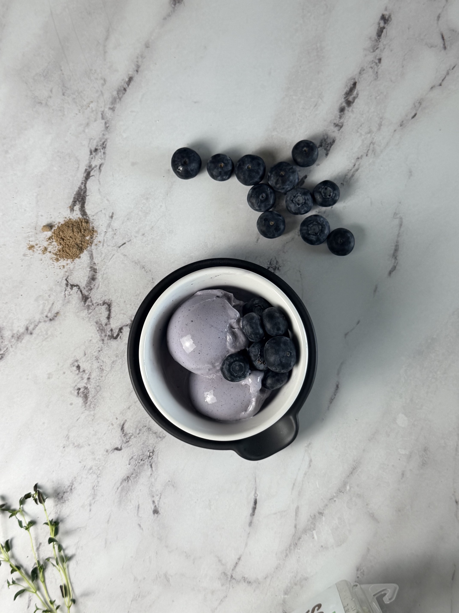 Blueberry protein ice cream scoops in a black bowl on a marble surface with fresh blueberries