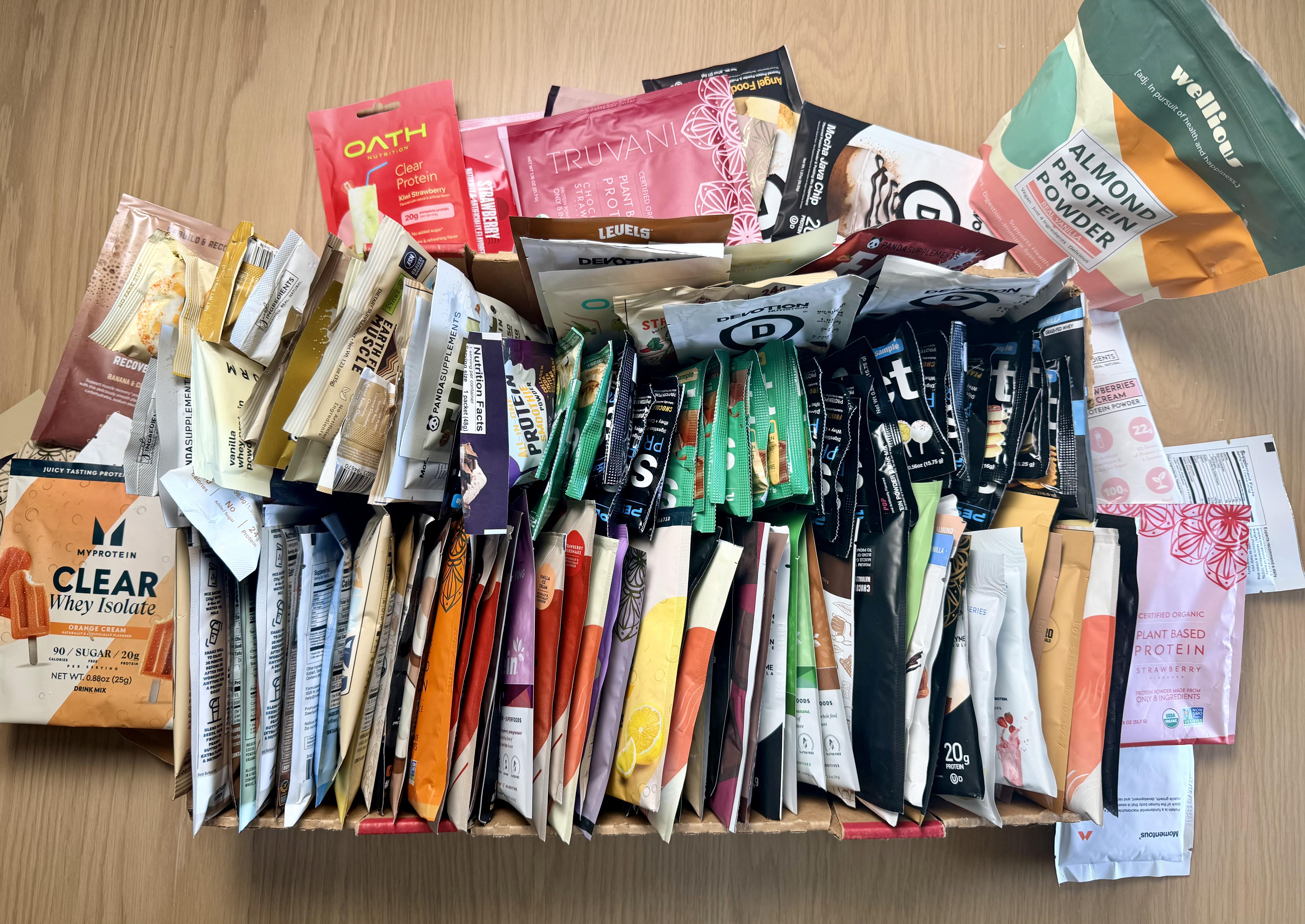 A large collection of protein powder sample packets from over 60 brands tested at The Pint Lab